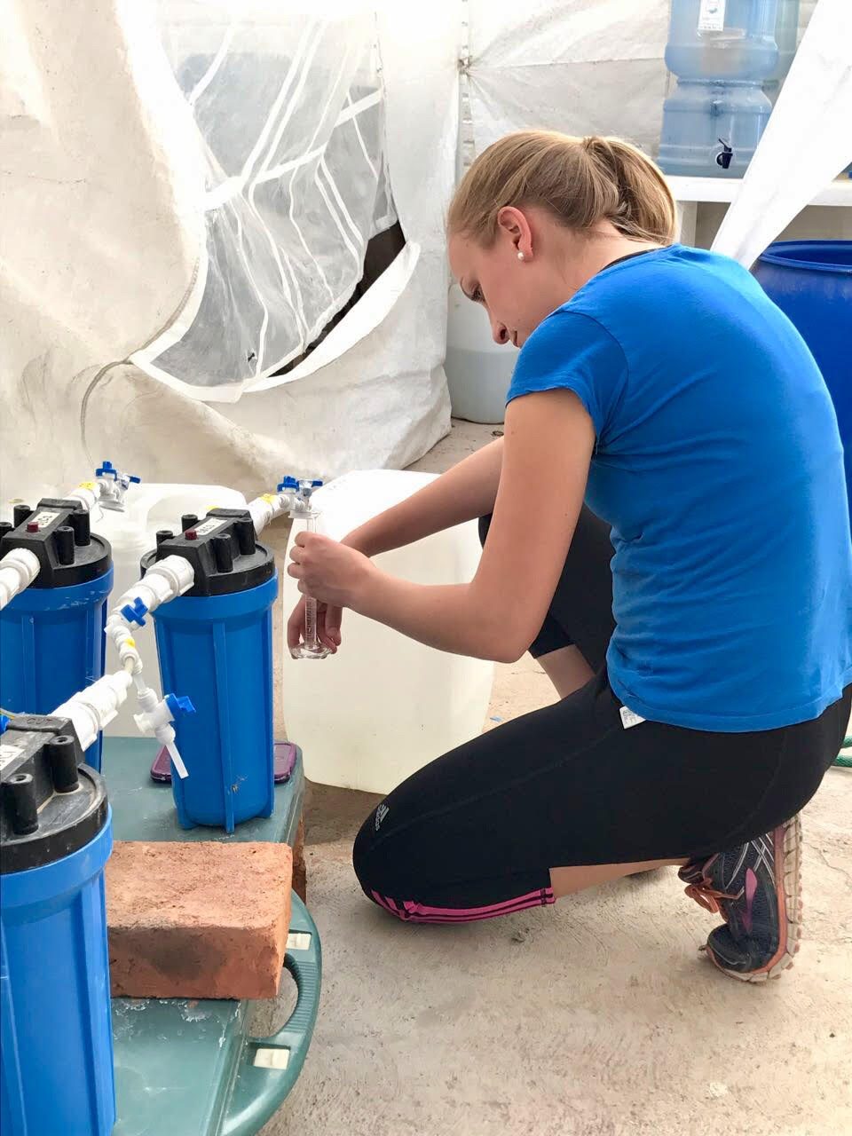 Sarah assembling a low-tech water filtration system from blue cartridge housings and plastic drums